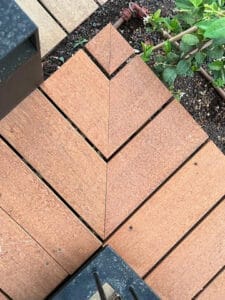 Wooden deck panels arranged in a chevron pattern next to a garden bed with green plants and soil, showcasing בניית דקים איכותית לצד צמחיה ירוקה.