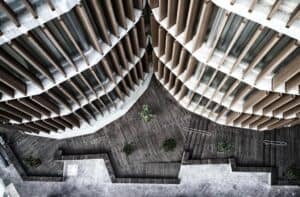 Aerial view of a modern building with wooden slats and geometric terraces, featuring several small trees and a wooden decked courtyard below showcasing התקנת דק במבוק for a natural, stylish look.
