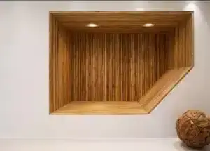 Rectangular wooden alcove with חיפוי במבוק, horizontal and vertical lines set into a white wall, featuring two ceiling lights and an angled side platform; a textured wooden sphere sits nearby on the floor.